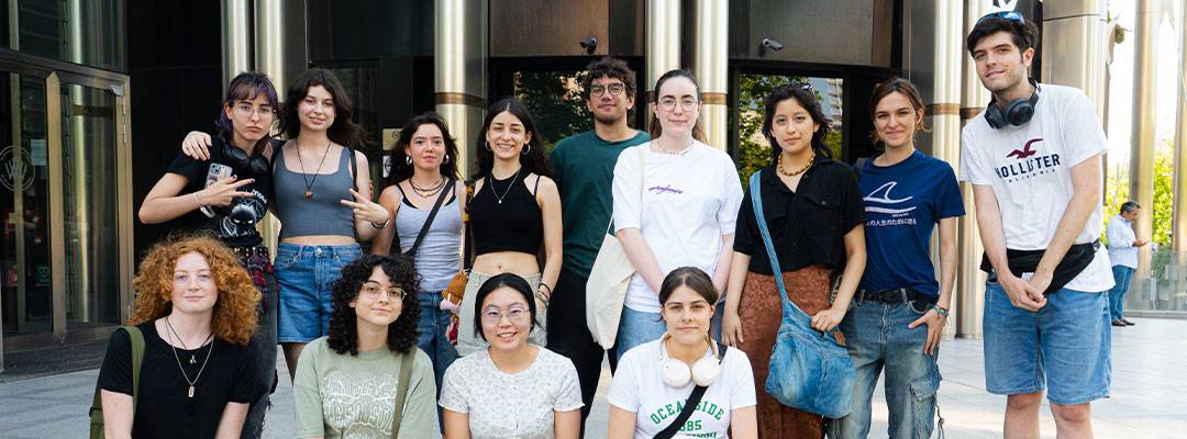 Un grupo de trece jóvenes posando juntos frente a un edificio moderno.