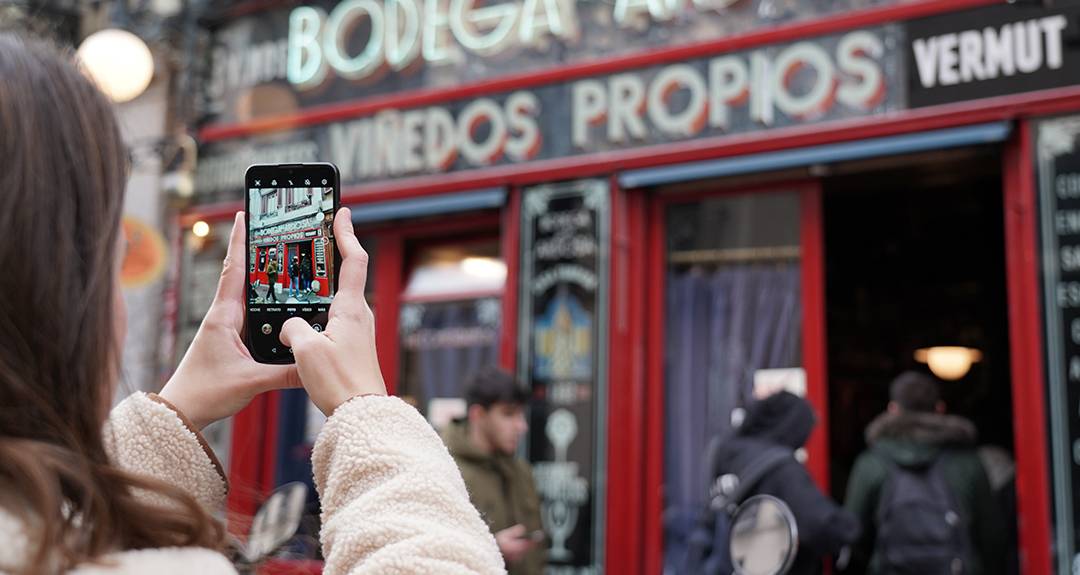 Una persona toma una fotografía con su teléfono frente a una bodega con letreros coloridos.