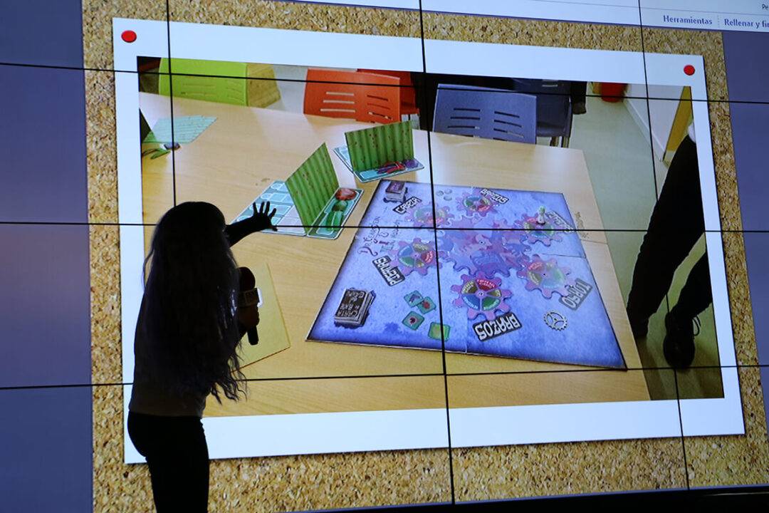 Una persona está presentando un juego de mesa en una pantalla grande.