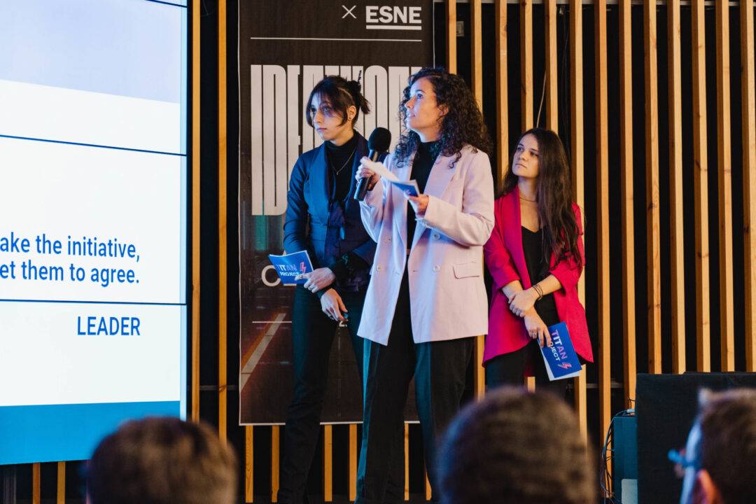 Una mujer habla en un evento mientras dos personas la escuchan atentamente.