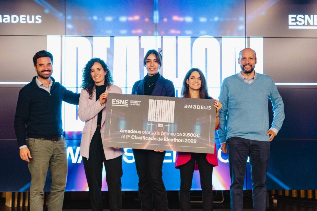 Un grupo de cinco personas sonríe mientras sostiene un cheque en un evento relacionado con un hackathon.