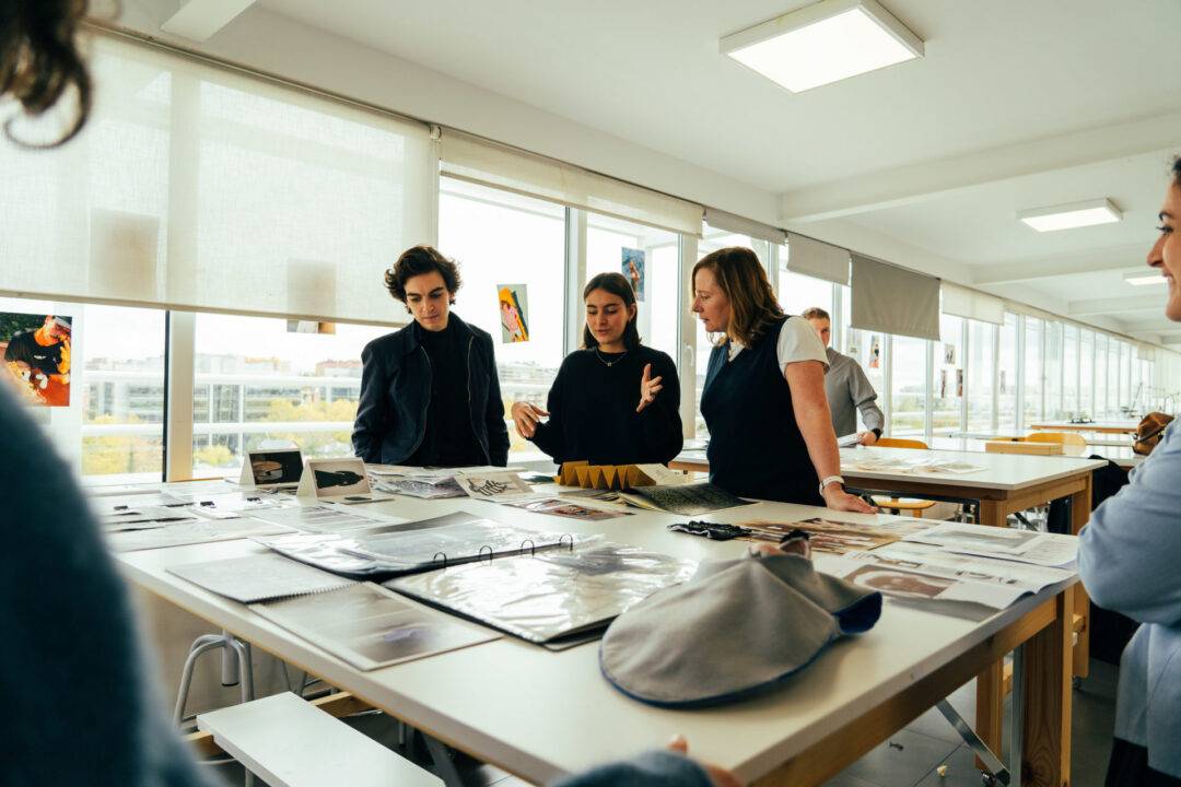 Un grupo de personas discute sobre proyectos en una sala luminosa con mesas llenas de documentos y materiales.