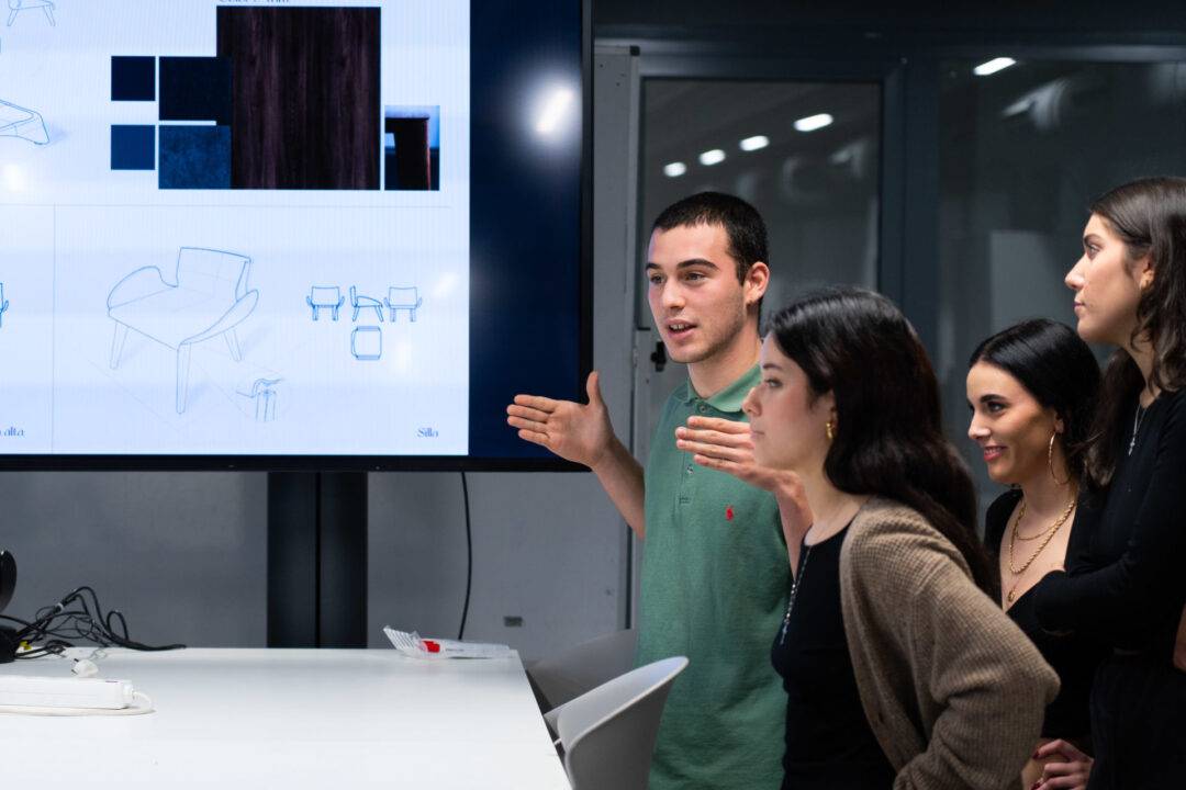 Un grupo de jóvenes observa una presentación en una pantalla mientras una persona habla gesticulando.