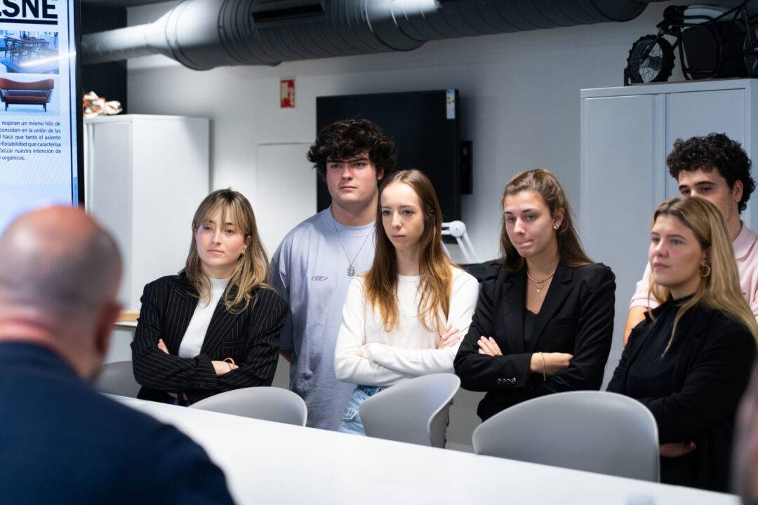 Un grupo de jóvenes observa atentamente a un presentador en un entorno de oficina moderna.