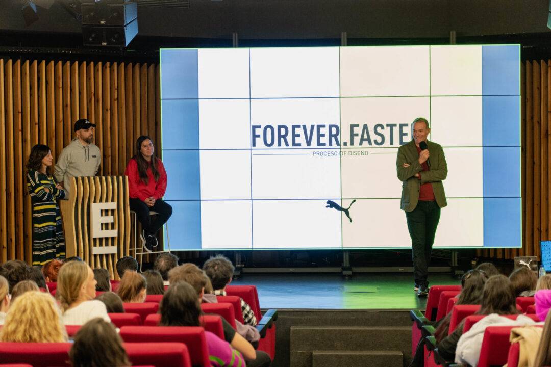 Un grupo de personas en un evento de presentación, con una pantalla grande que muestra el texto 'FOREVER.FASTER'.