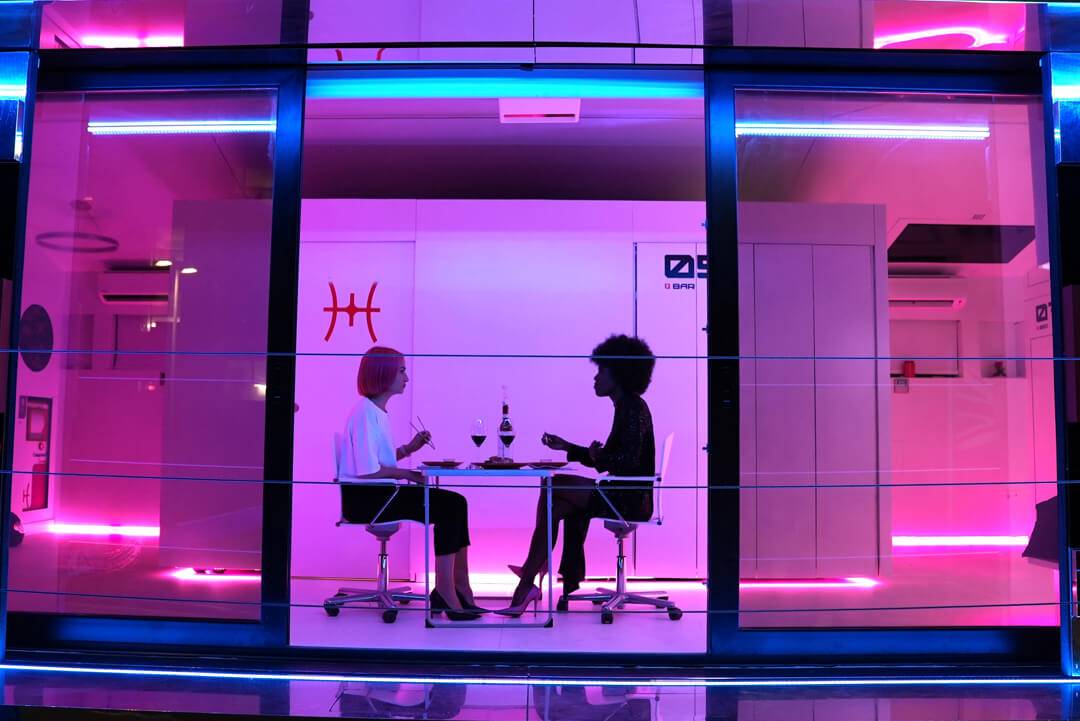 Dos mujeres conversan en un elegante ambiente iluminado con luces de neón.