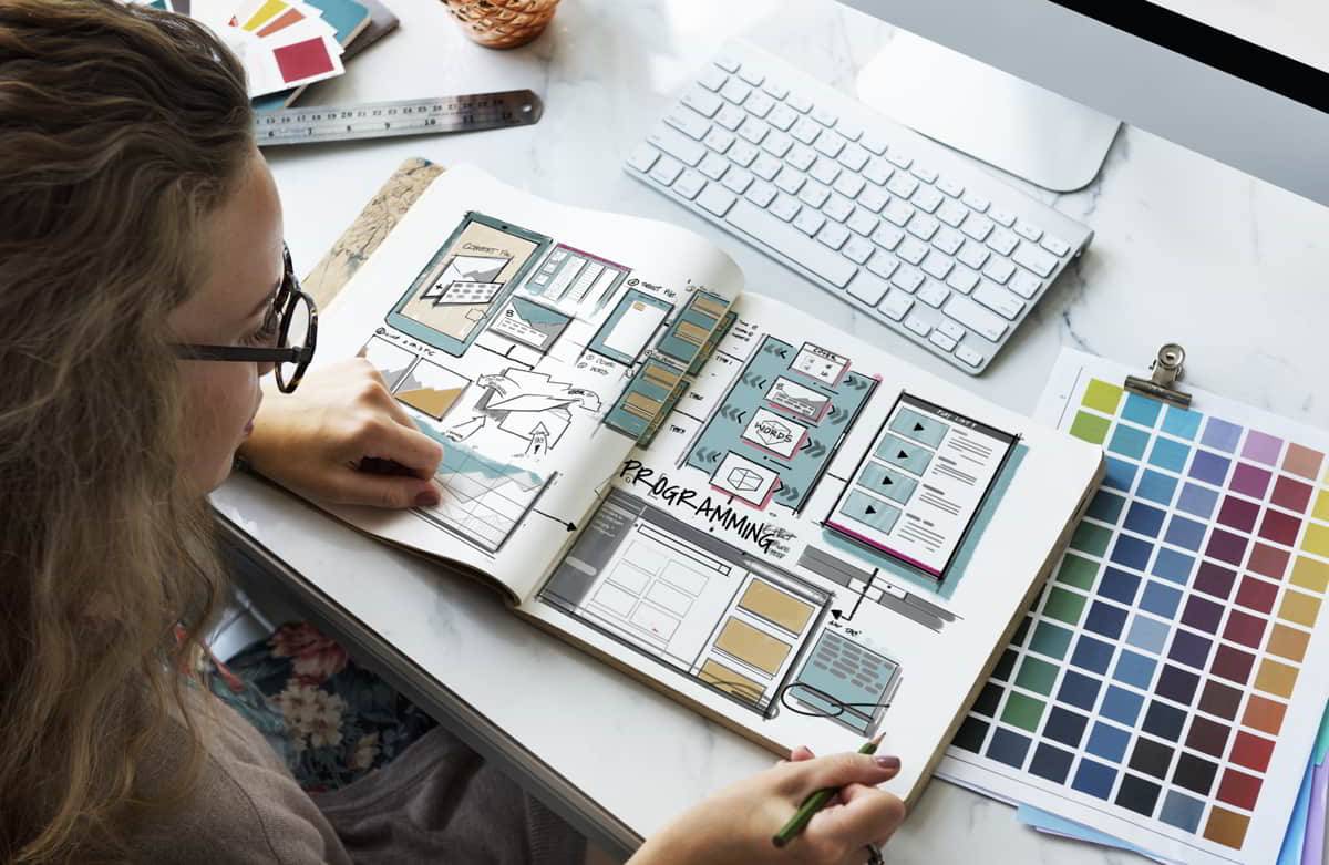 Una persona está trabajando en un cuaderno de bocetos mientras utiliza una computadora en un entorno de diseño.