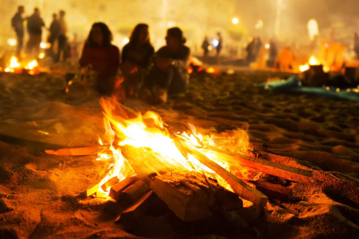 Una fogata brilla en la playa, rodeada de personas que disfrutan del ambiente nocturno.