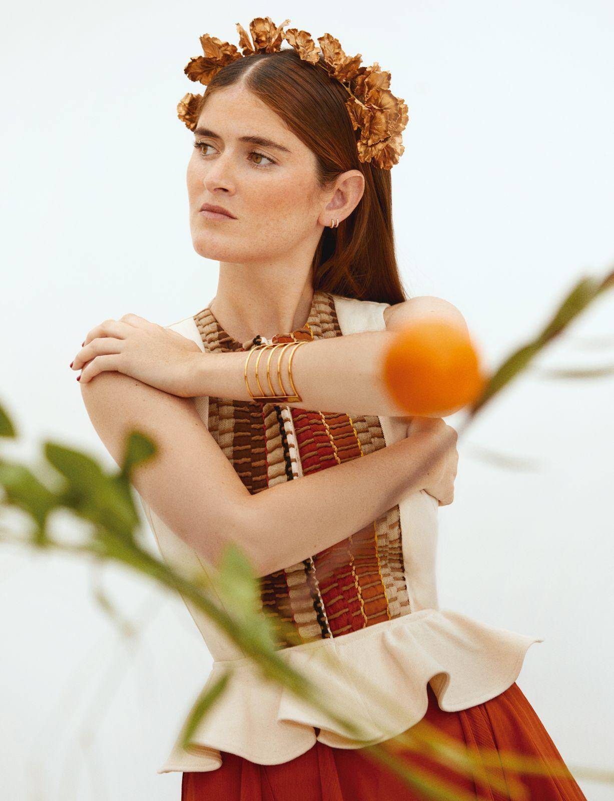 Una mujer posando con un vestido de estilo bohemio y una corona de flores en un fondo minimalista.