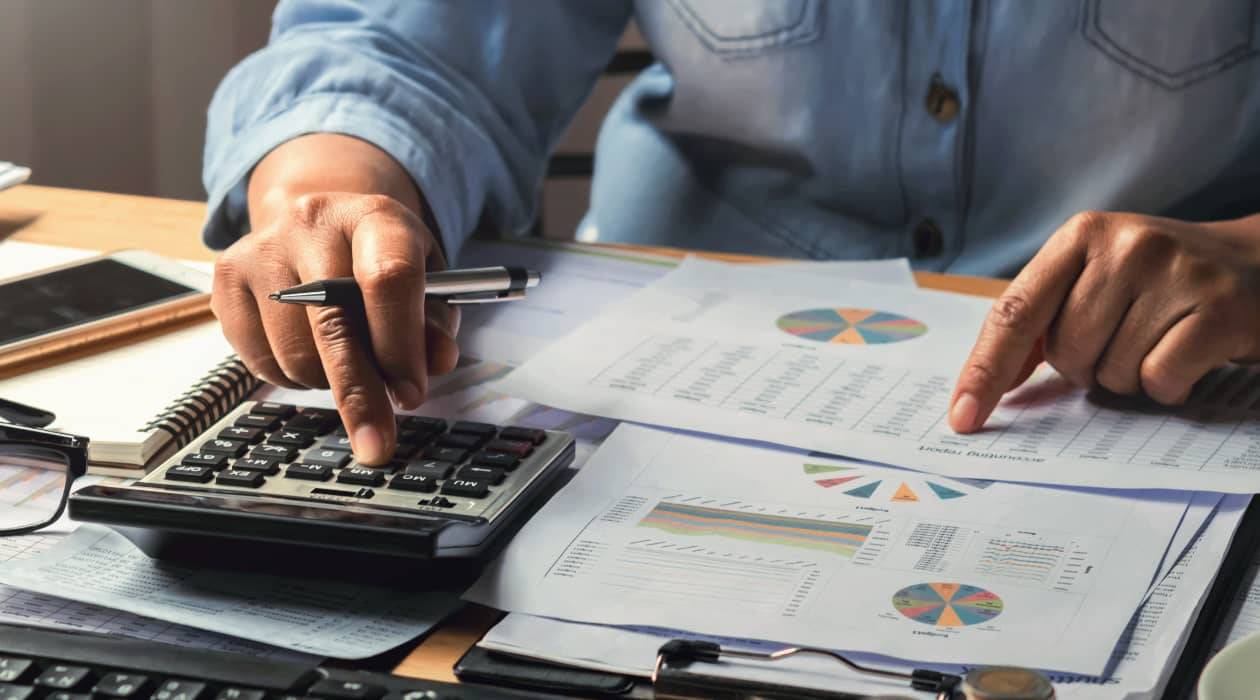 Una persona está utilizando una calculadora mientras revisa documentos con gráficos y datos financieros.