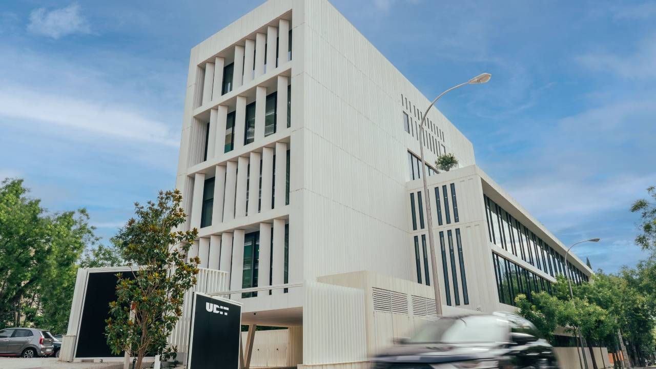 Edificio moderno con fachada blanca y vegetación alrededor.