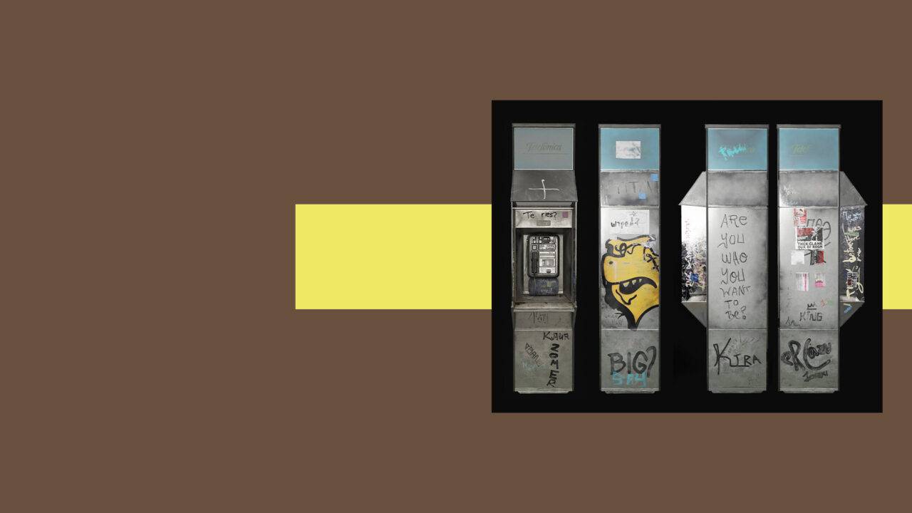Una serie de cabinas telefónicas con grafitis en una pared de fondo marrón.