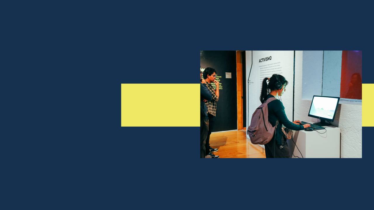 Una persona está interactuando con un ordenador en una exposición, mientras otra persona observa en el fondo.