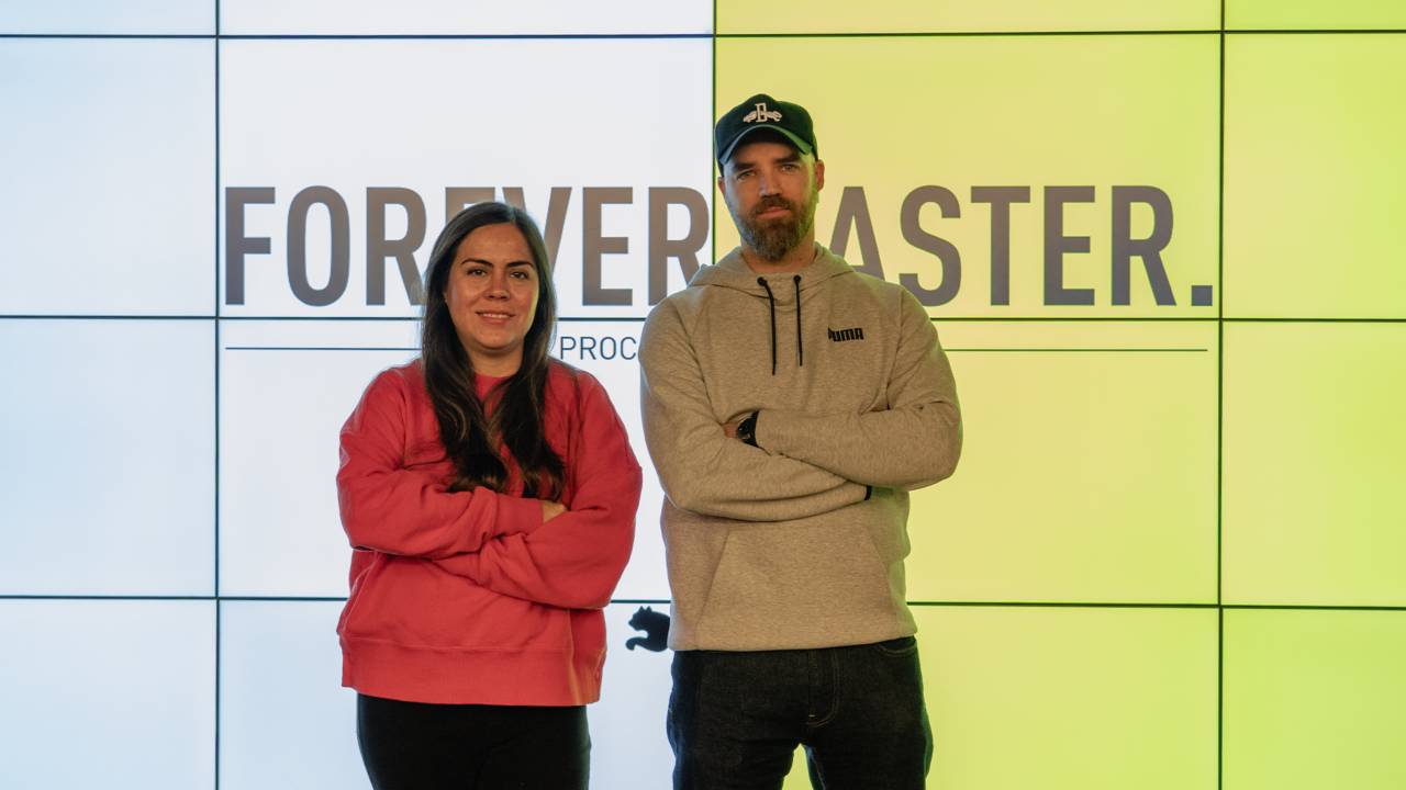 Dos personas posan frente a una pantalla con el texto 'FOREVER MASTER'.