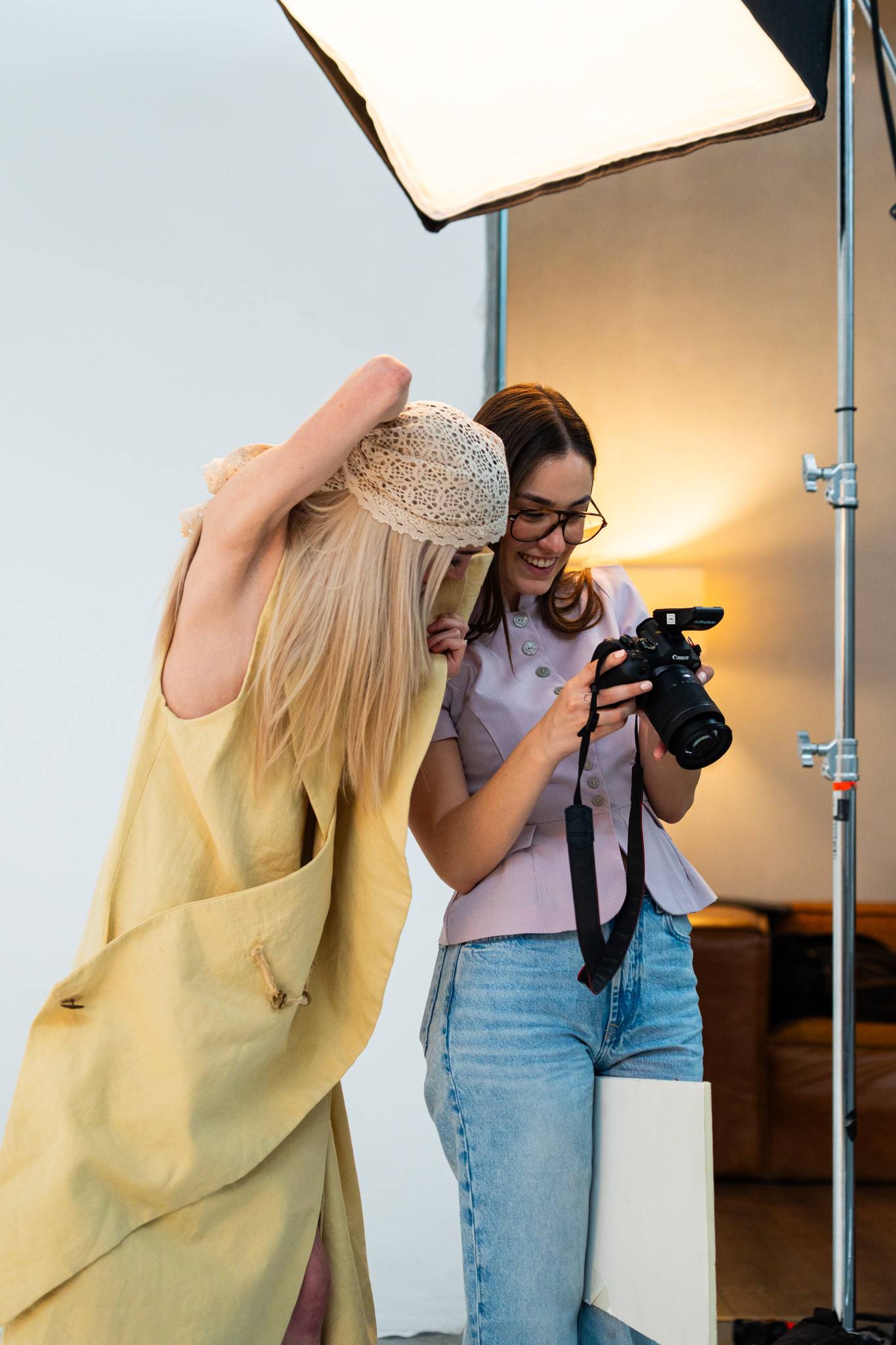 Dos mujeres se ríen y comparten un momento divertido mientras revisan fotos en una cámara en un estudio.