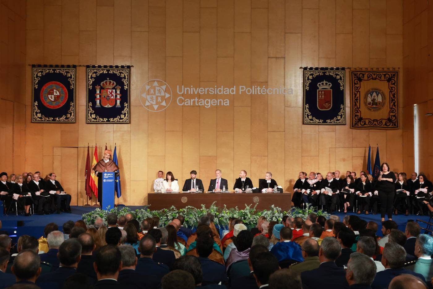 Ceremonia académica en la Universidad Politécnica de Cartagena con autoridades en el podio y graduados en la audiencia.