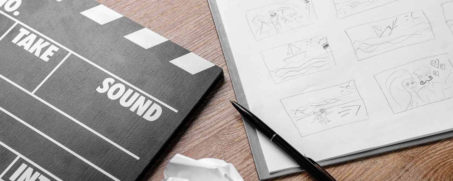 La imagen muestra una claqueta de cine junto a una hoja con bocetos y un bolígrafo.