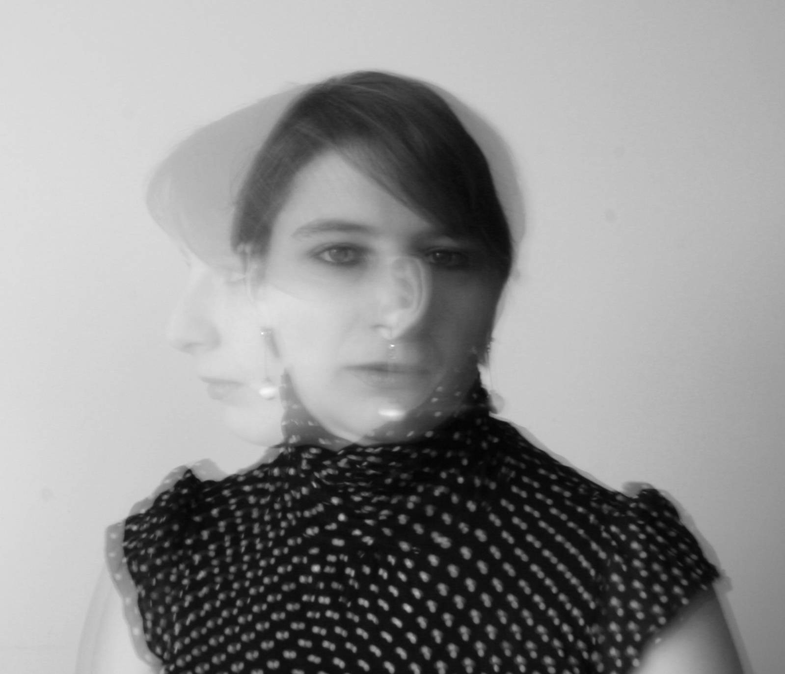 La imagen muestra un retrato en blanco y negro de una mujer con un efecto de movimiento o desenfoque en su rostro.