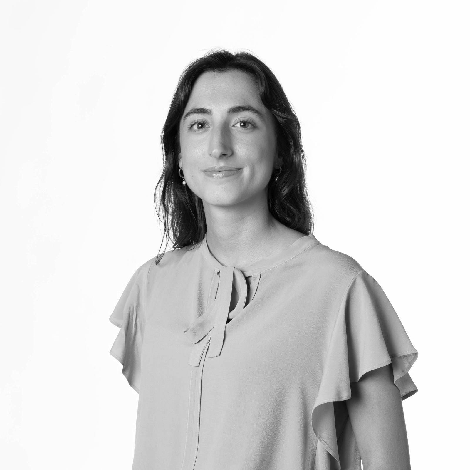 Una persona sonriente posando con una blusa clara en un fondo blanco.