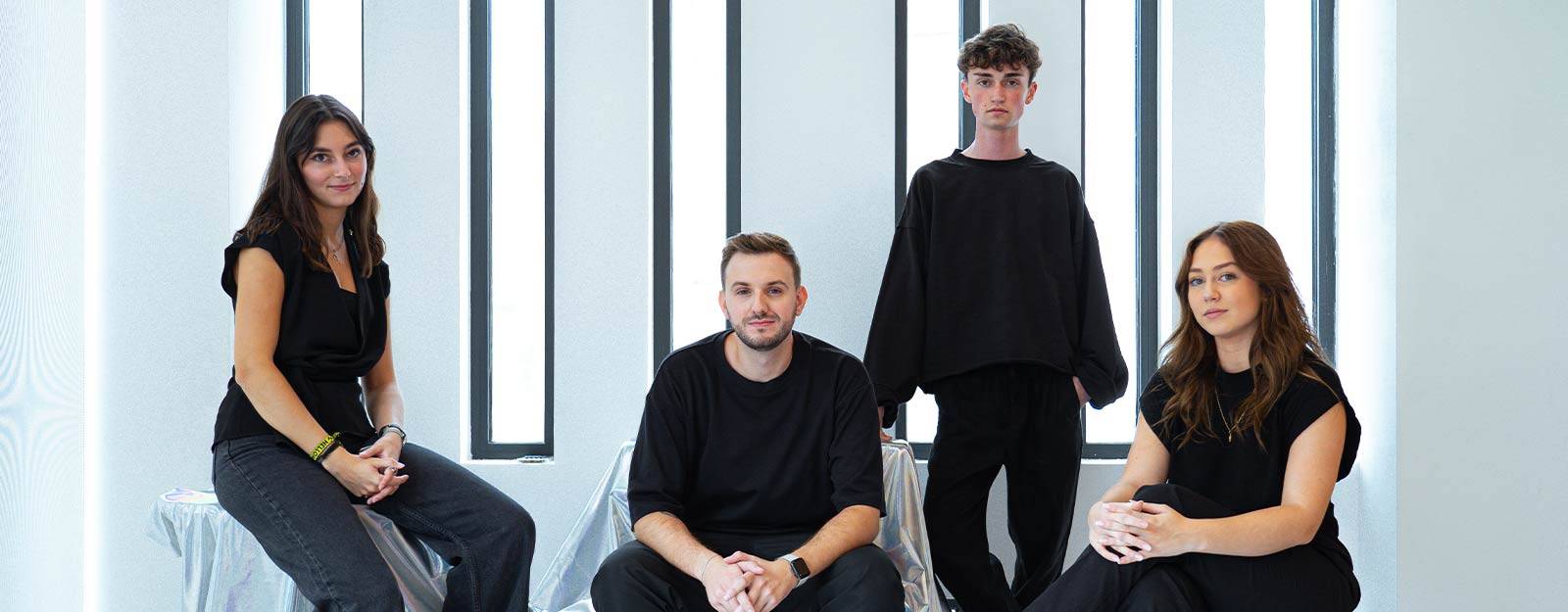 Cuatro personas vestidas de negro posan en un entorno moderno y minimalista.