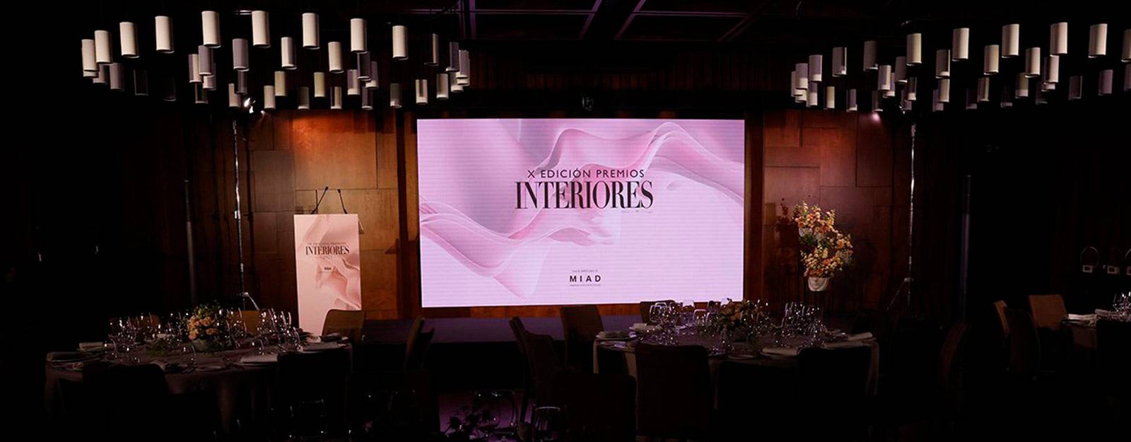 La imagen muestra un elegante salón con una pantalla que presenta un evento relacionado con interiores.