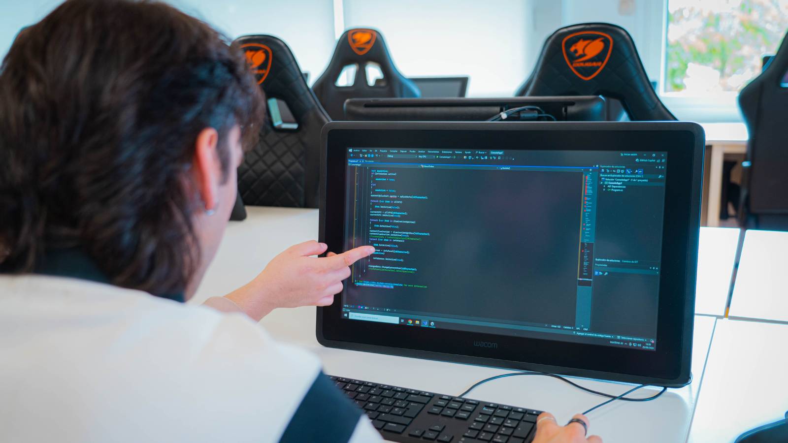 Una persona señala la pantalla de una computadora que muestra código en una sala de clases.