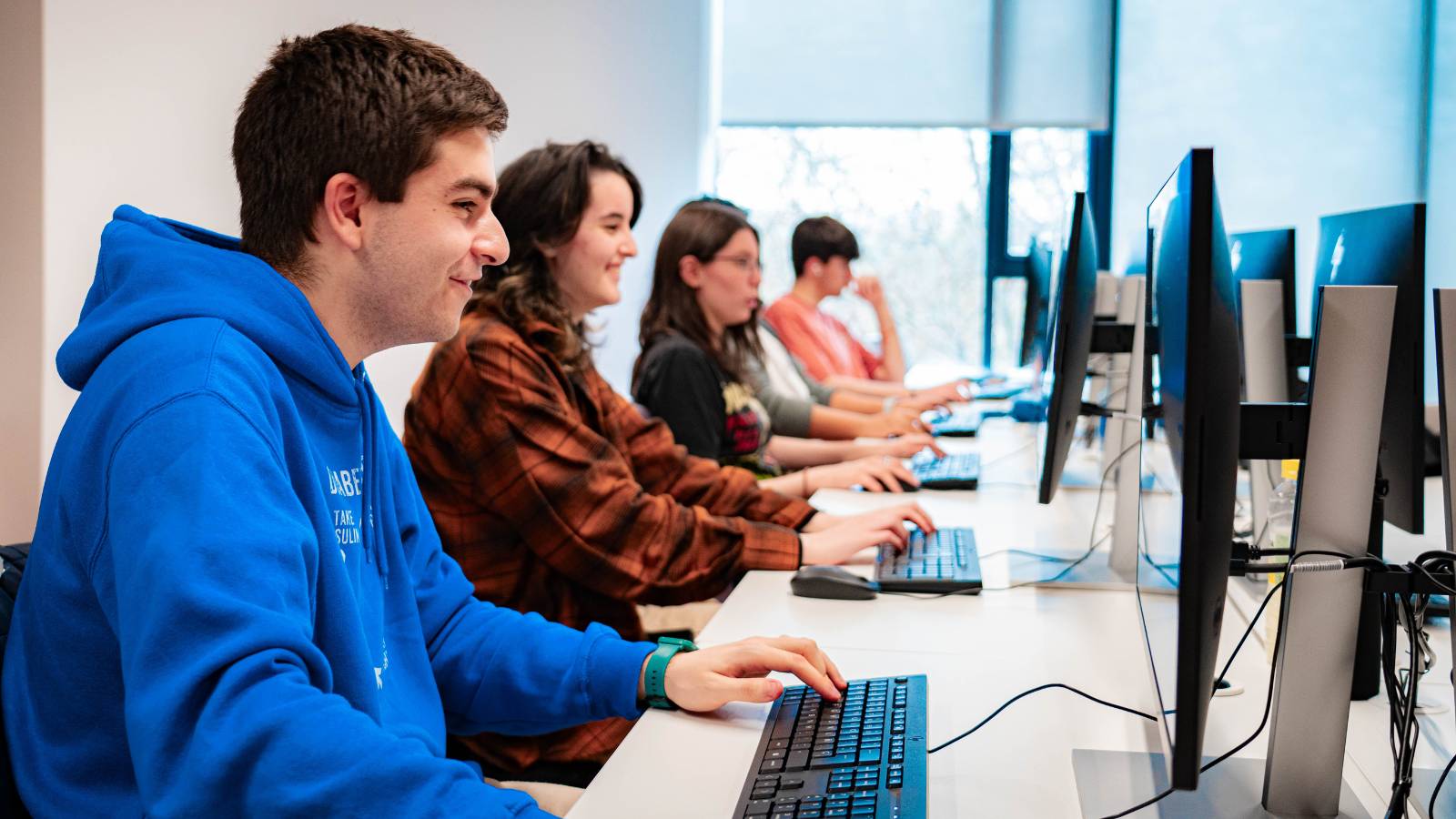 Un grupo de estudiantes sentado frente a computadoras en un aula.