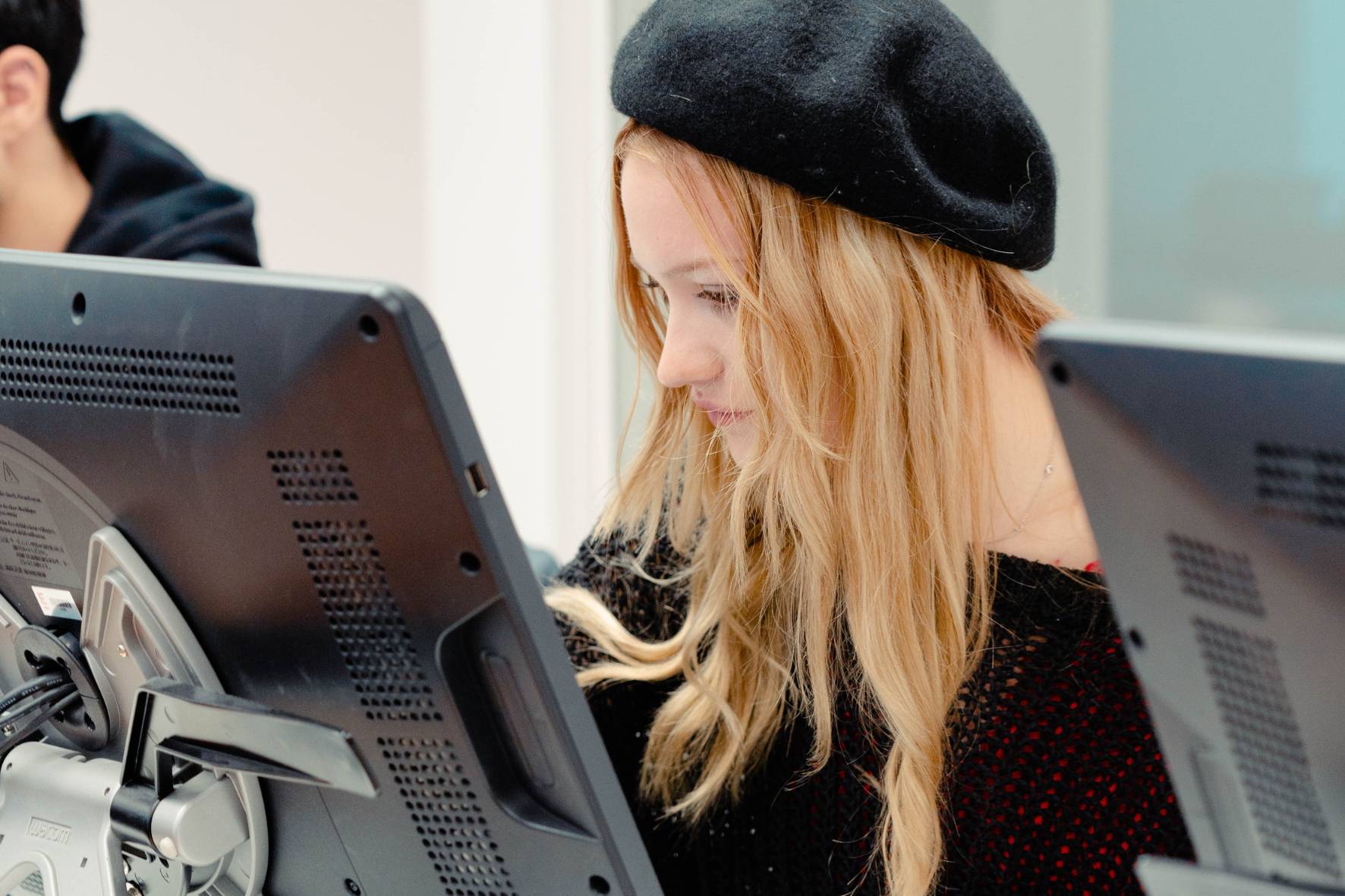 Una joven con sombrero se concentra en la pantalla de una computadora.