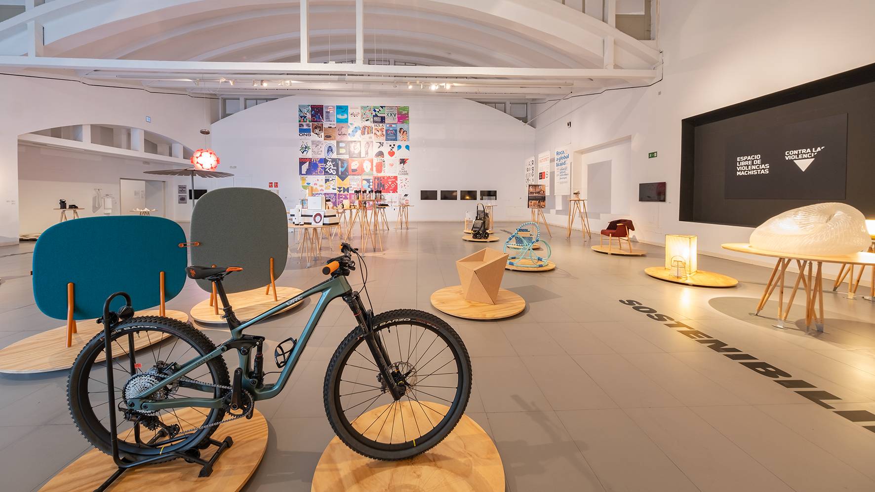 Una exposición moderna que presenta una bicicleta y diversos objetos de diseño en un espacio amplio y luminoso.