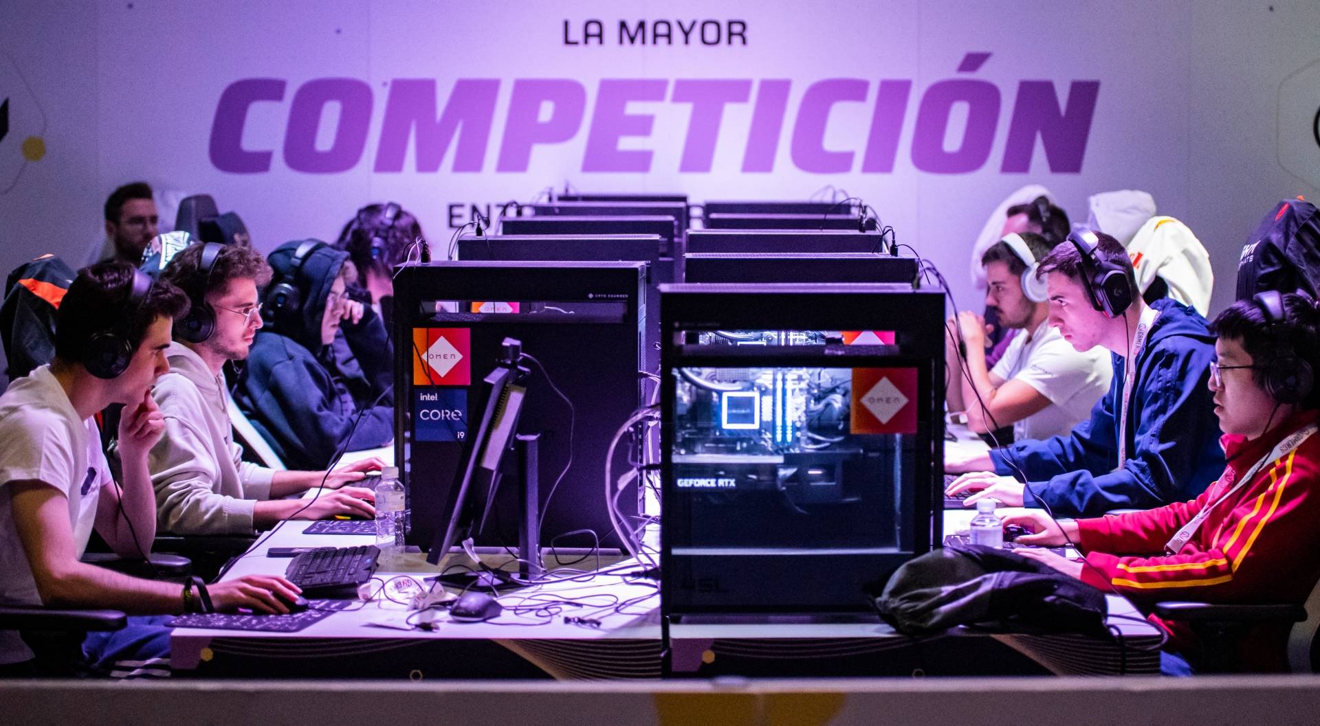 Una competición de videojuegos donde varias personas juegan en computadoras junto a un cartel que dice 'LA MAYOR COMPETICIÓN'.
