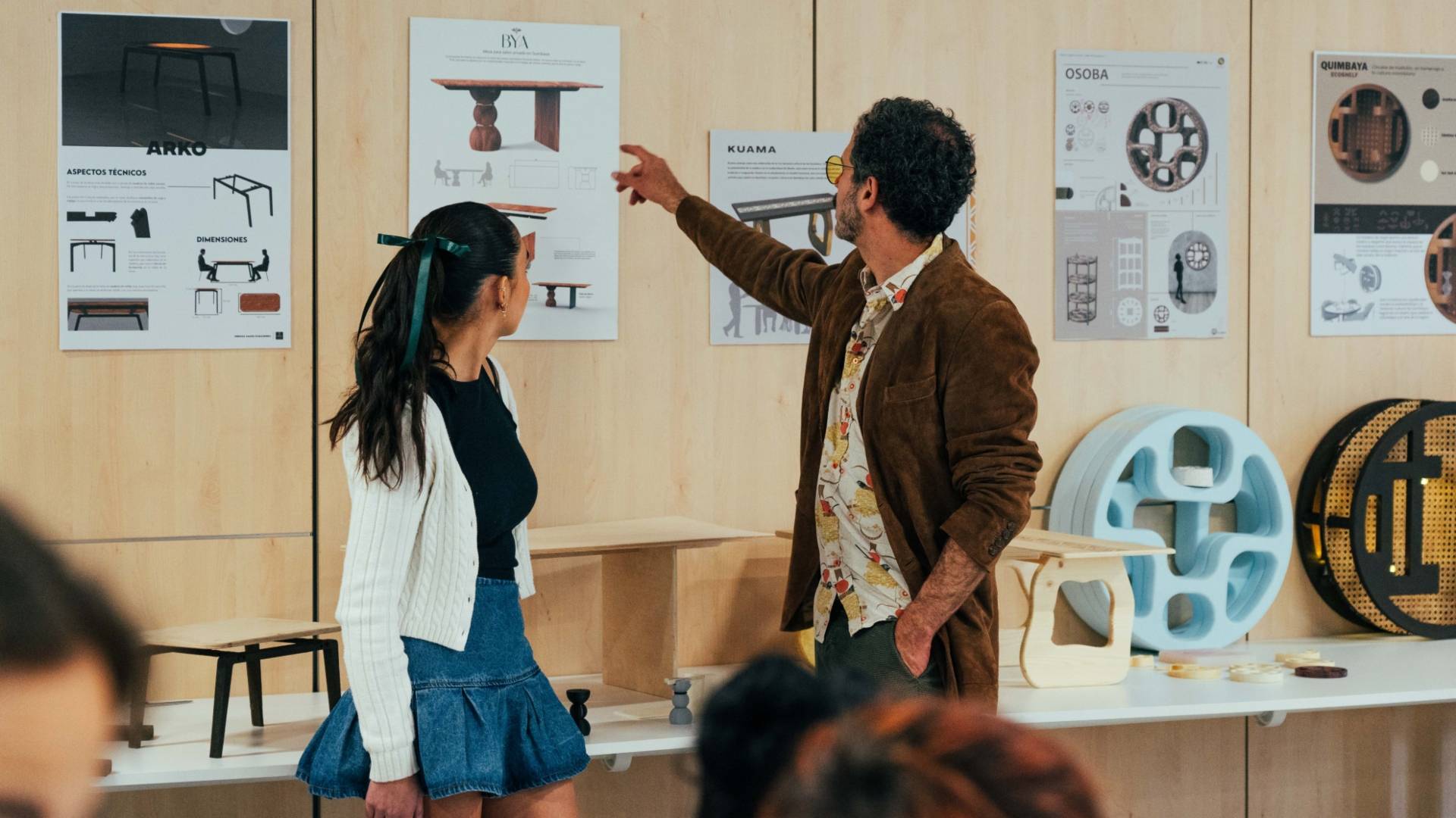 Dos personas discuten sobre diseños de mesas en un entorno de exhibición.