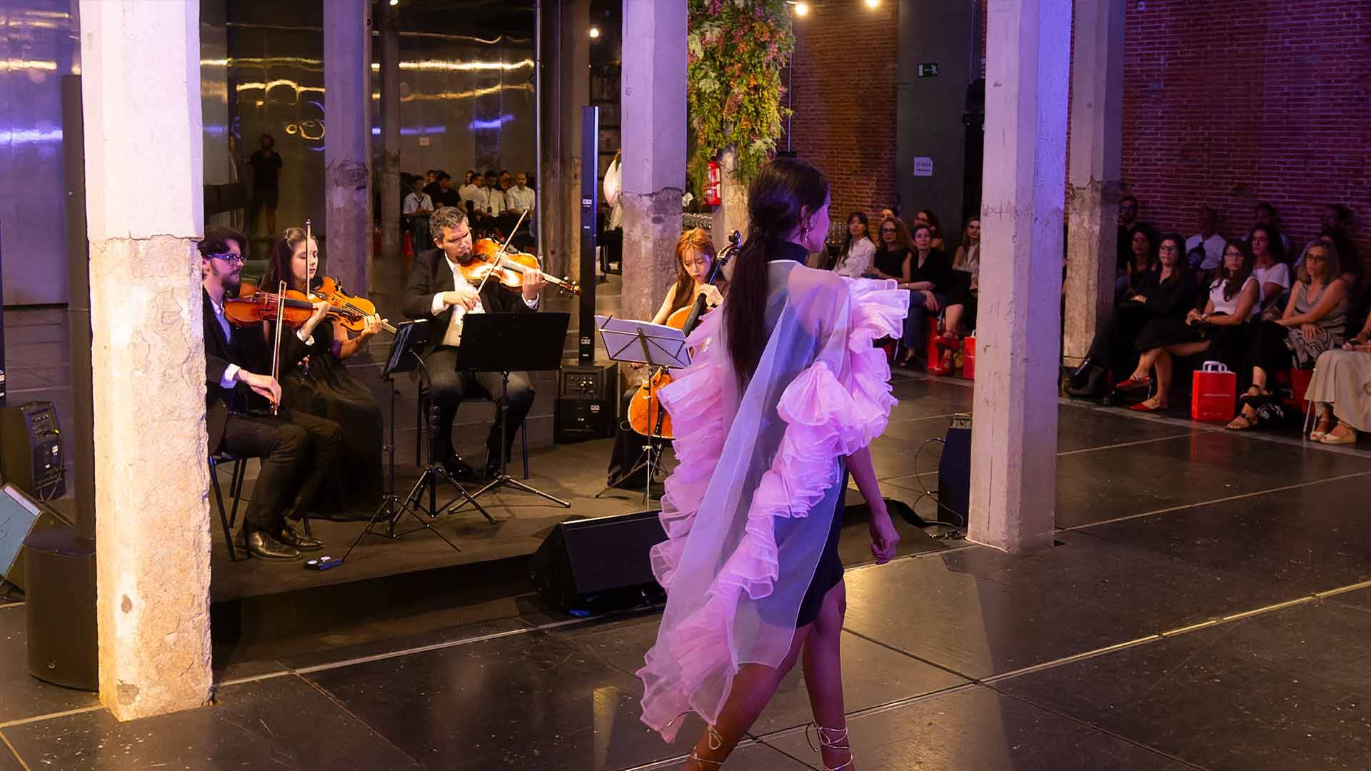 Una modelo desfila en una pasarela mientras un cuarteto de cuerdas toca música de fondo.