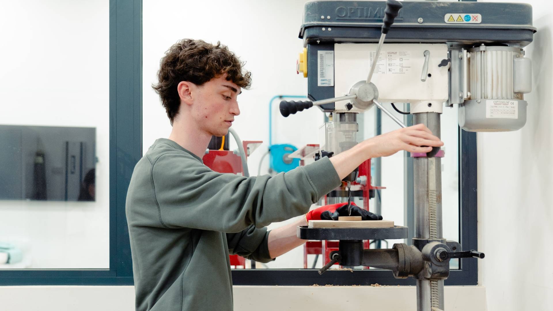 Un joven está operando una máquina de taladrar en un entorno de laboratorio.