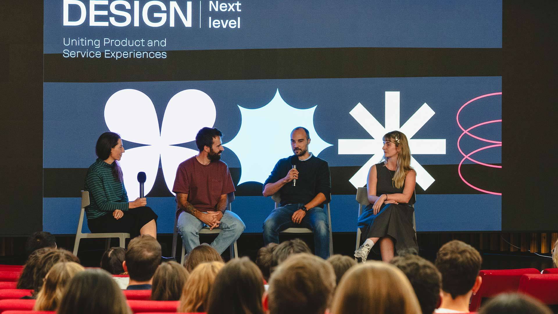 Un panel de discusión sobre diseño con cuatro participantes sentados frente a una audiencia.