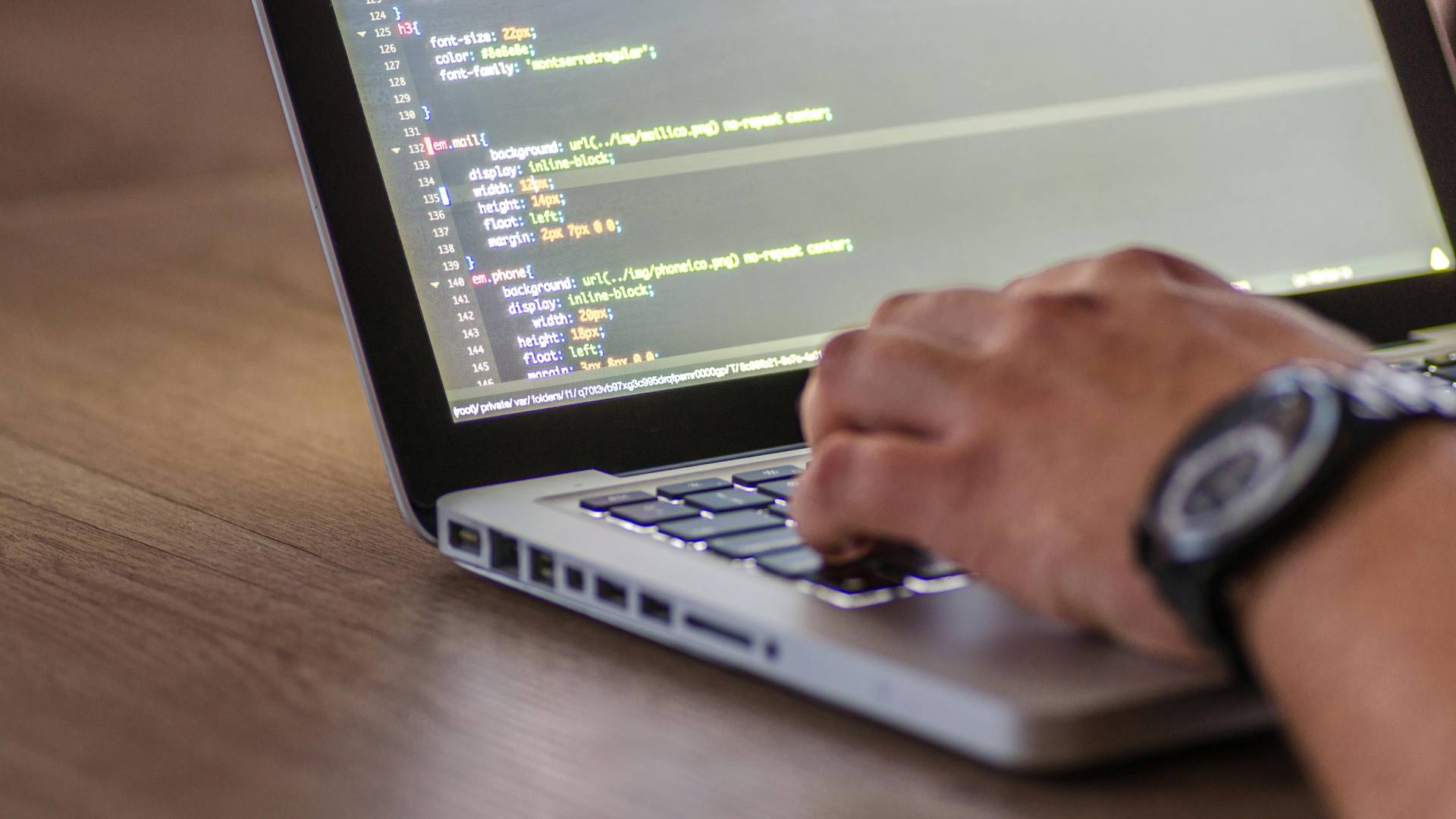 Una persona está programando en una computadora portátil con código visible en la pantalla.