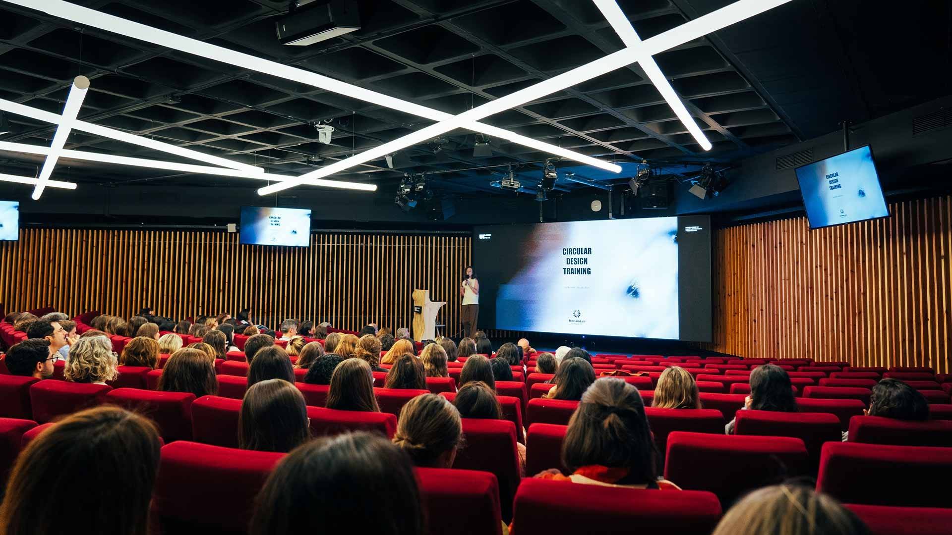 Una sala de conferencias llena de personas escuchando a un ponente.
