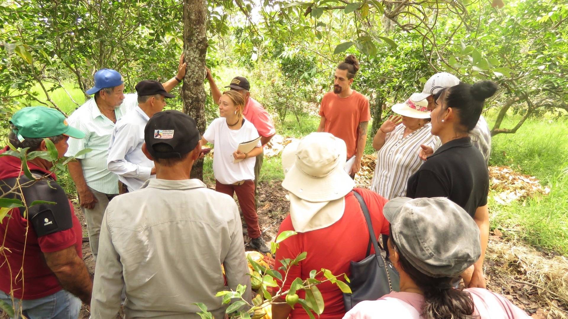 Un grupo de personas se reúne en un paisaje natural para recibir una charla sobre cultivos.