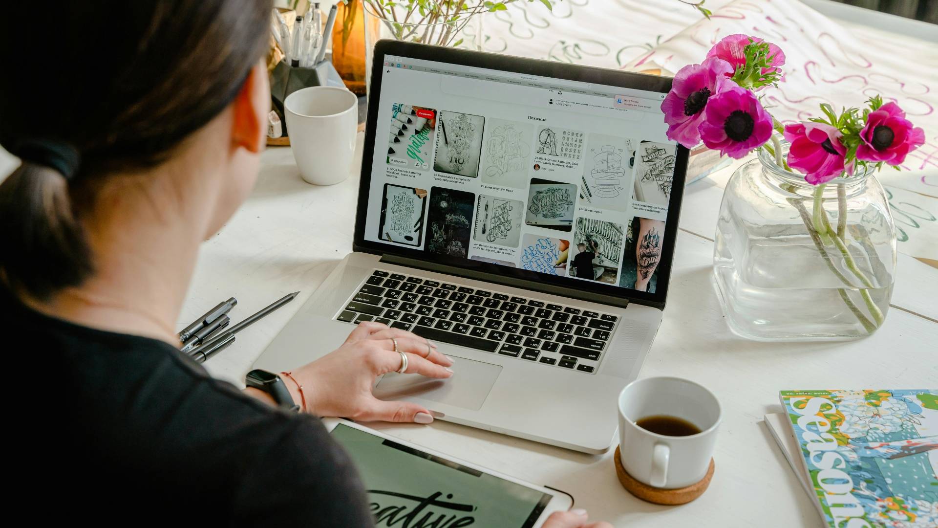 Una persona trabaja en su computadora portátil rodeada de plantas y flores, con una taza de café al lado.
