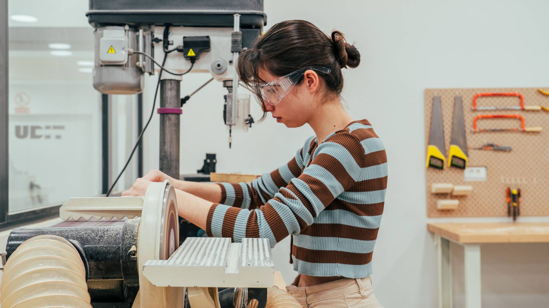 Una joven trabaja concentrada en una máquina de taller en un entorno de fabricación.