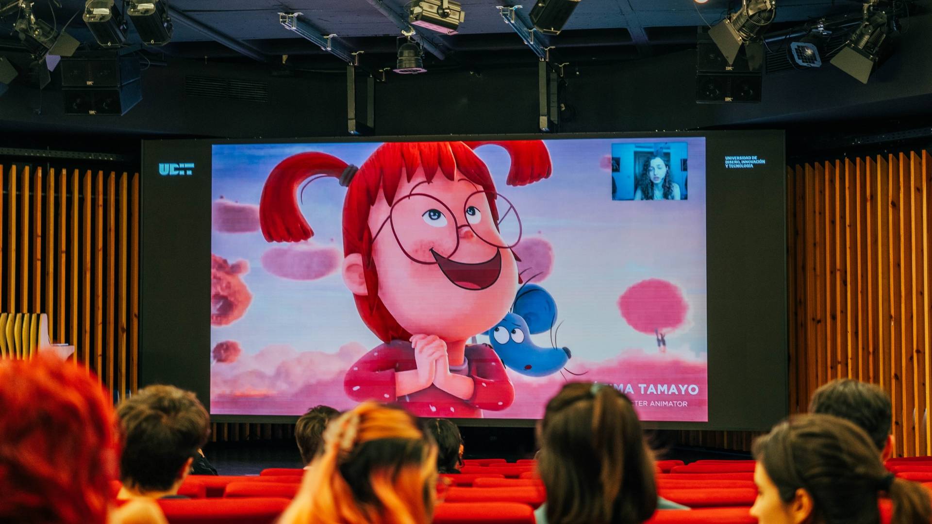 Una proyección animada en una sala con asistentes, mostrando a un personaje de dibujos animados con pelo rojo y gafas.