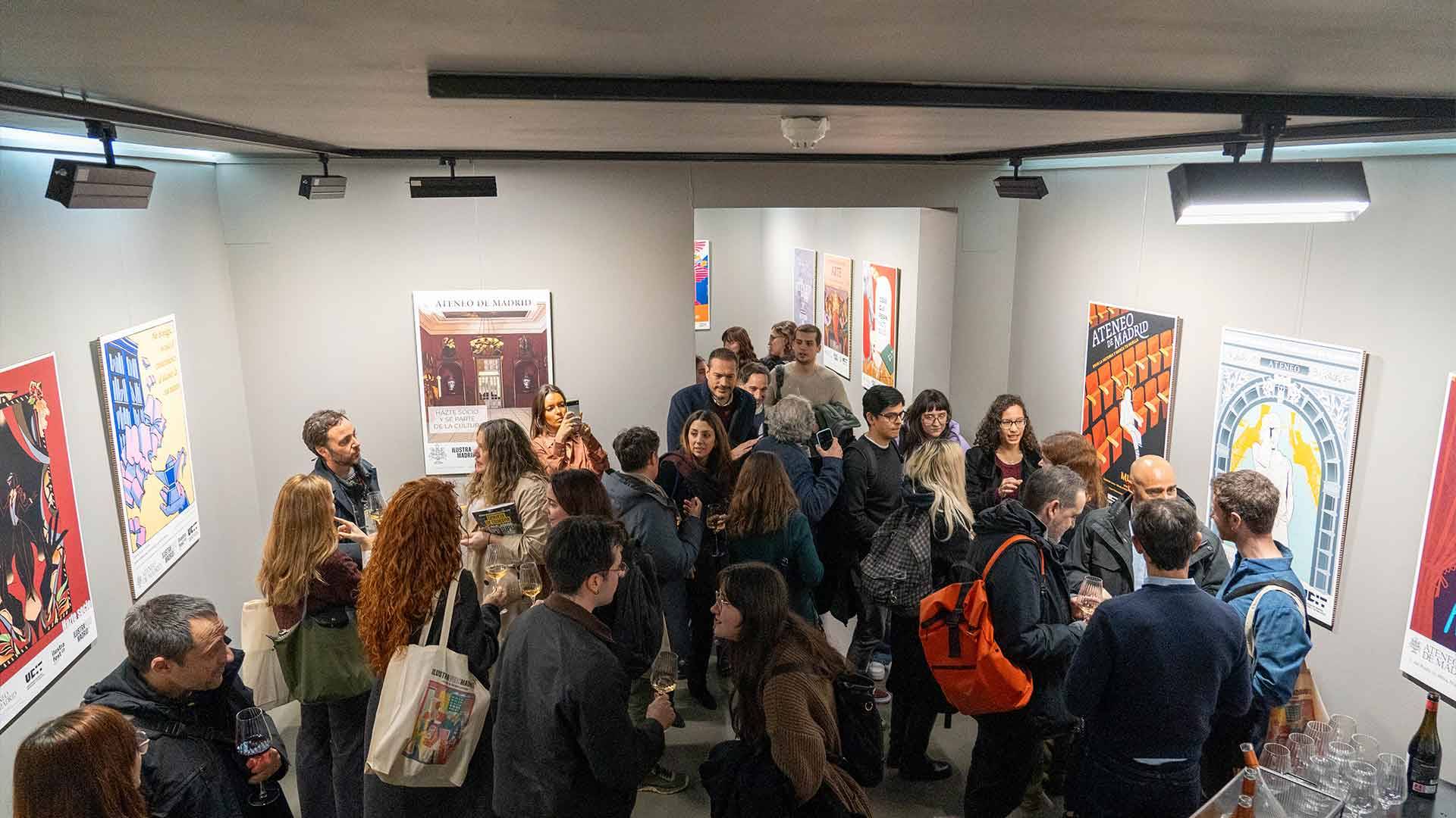 Una multitud de personas charlando y disfrutando en una exposición de arte con carteles en las paredes.