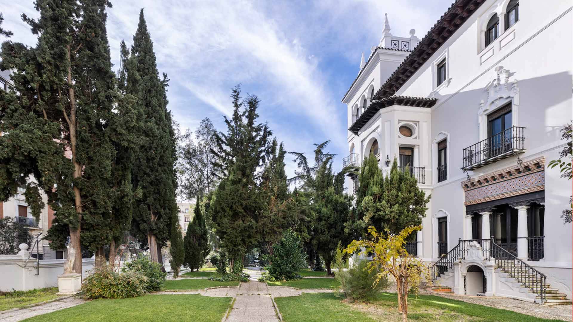 Vista de un jardín con árboles y una finca de estilo arquitectónico clásico al fondo.