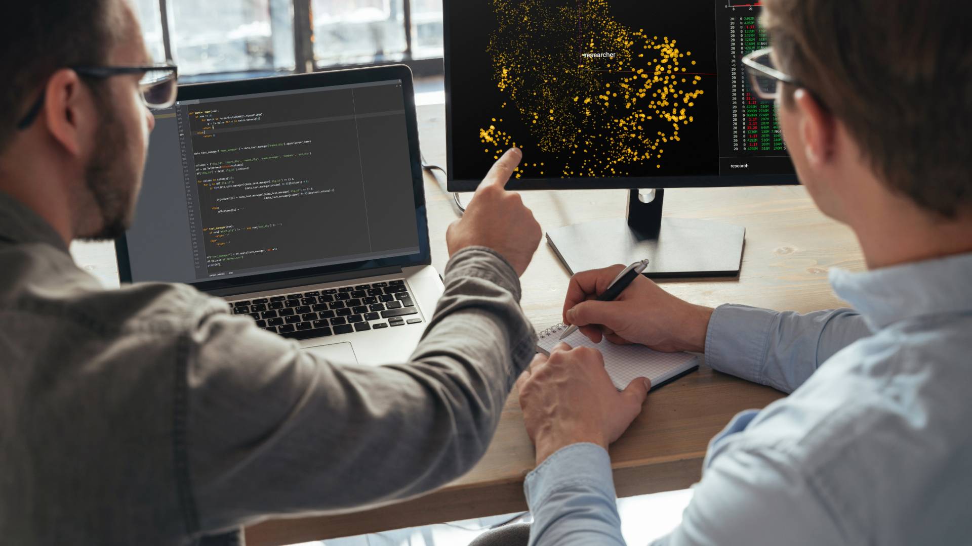 Dos personas analizando datos en pantallas de computadora en un entorno de oficina.