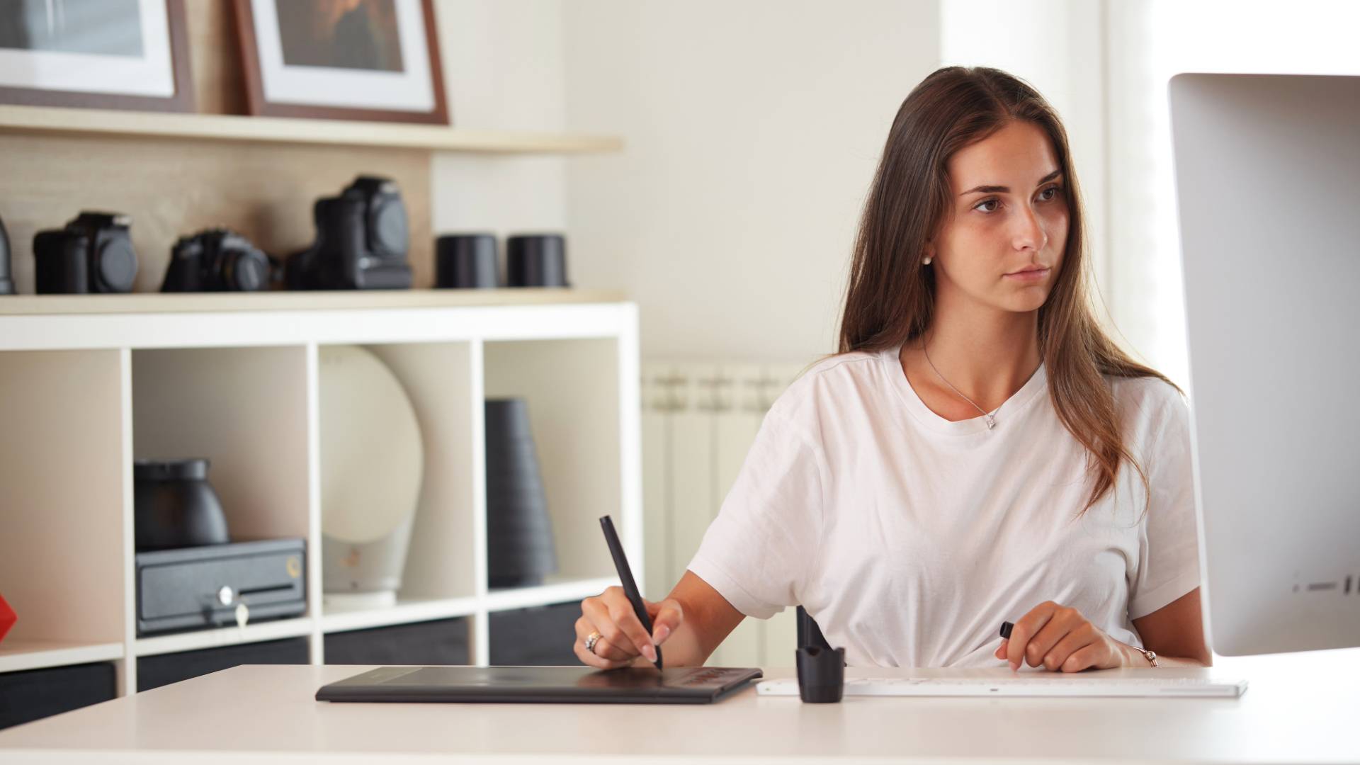 Una joven diseñadora trabaja concentrada en su mesa con una tableta gráfica y una computadora.