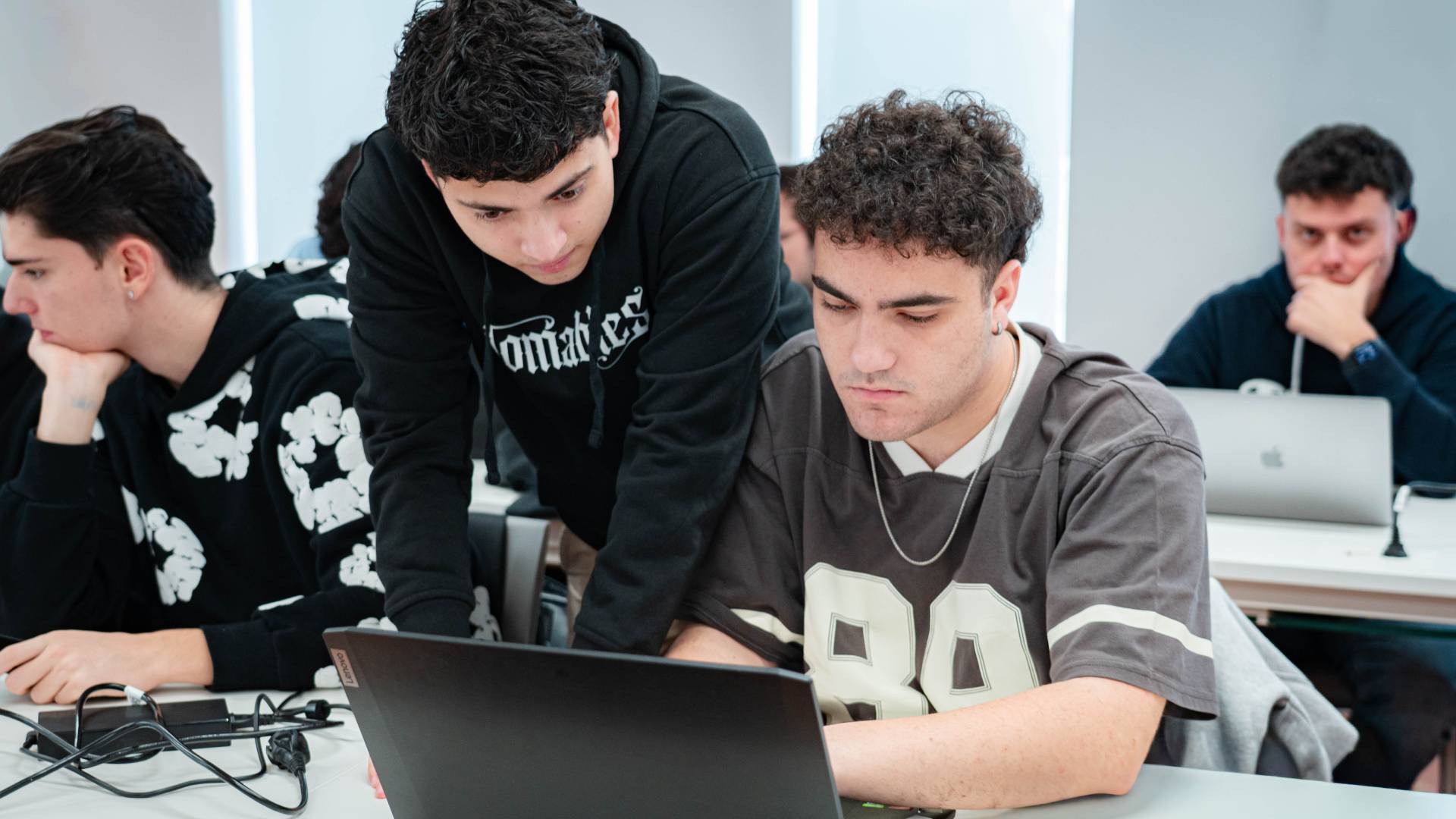 Dos estudiantes colaboran en un proyecto frente a una computadora portátil en un aula.