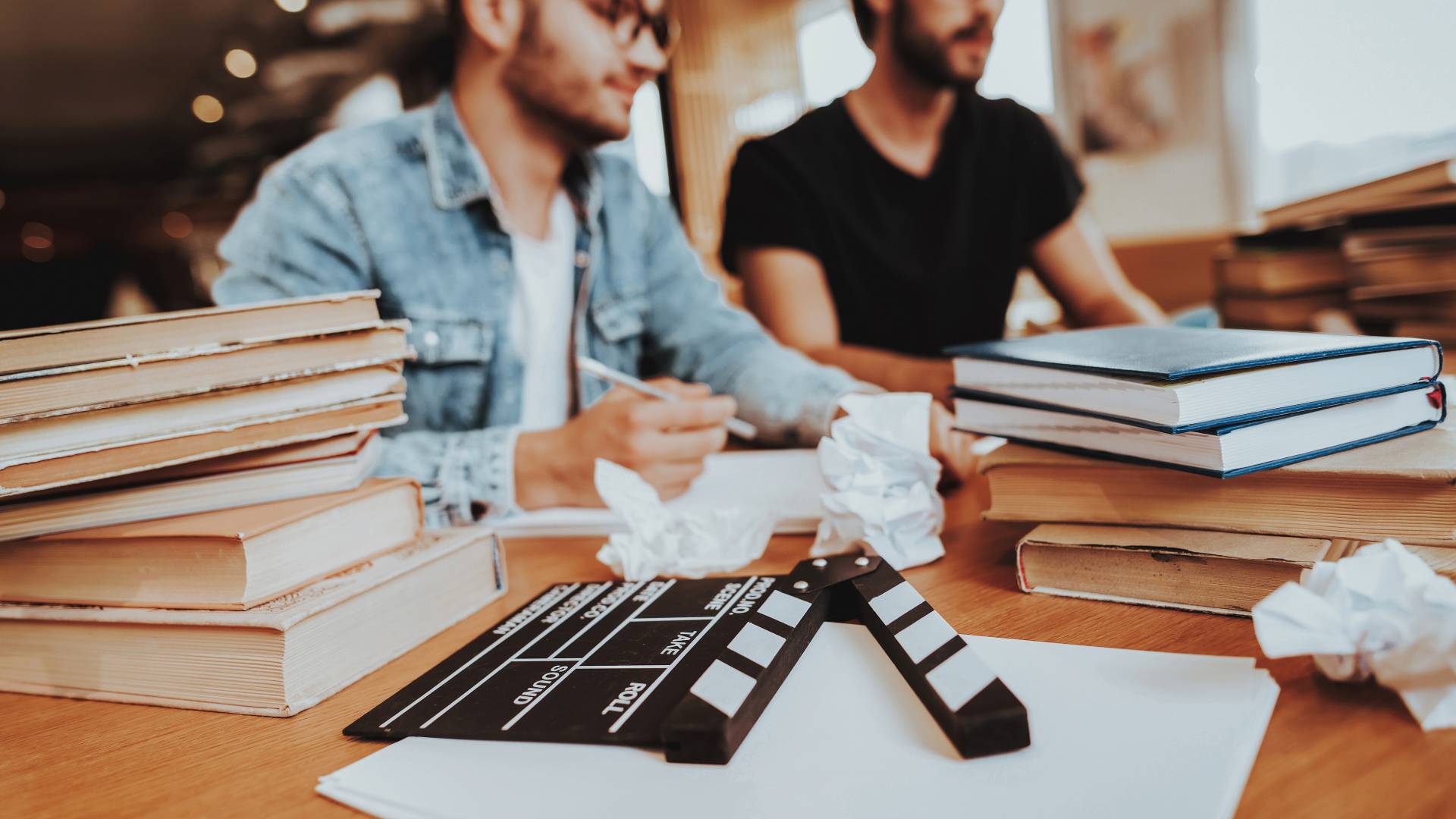 Dos hombres trabajan en un proyecto rodeados de libros y material de filmación.