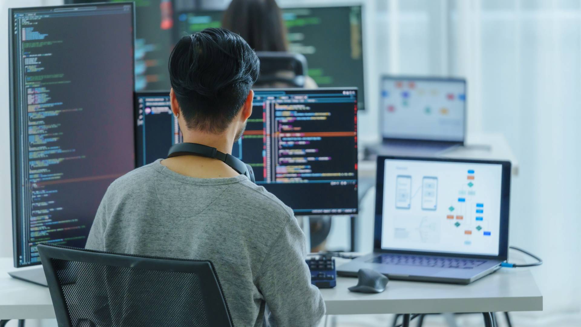 Una persona está programando frente a múltiples pantallas de computadora en un entorno de trabajo moderno.