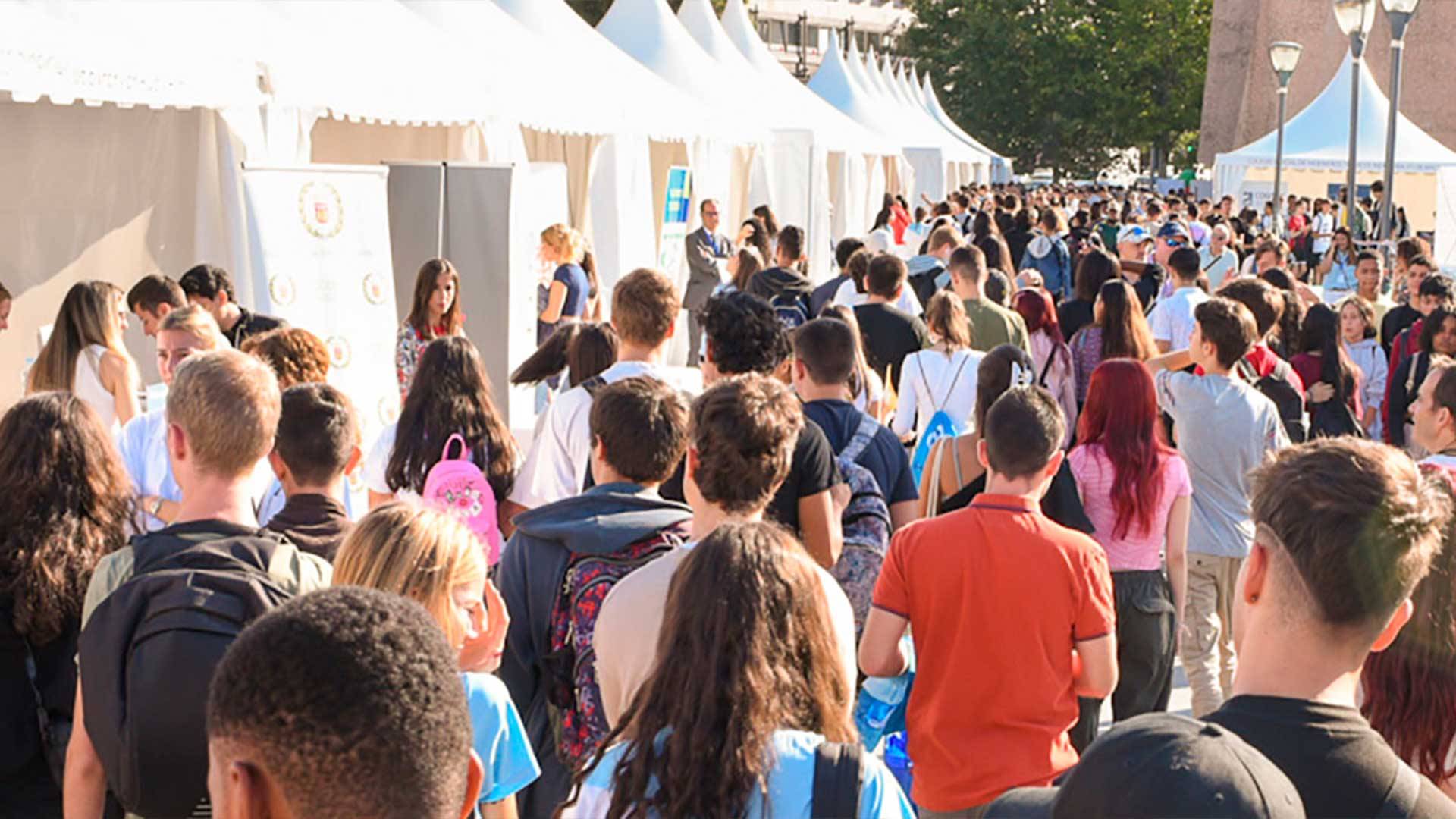 Una multitud de jóvenes caminando hacia carpas en un evento al aire libre.