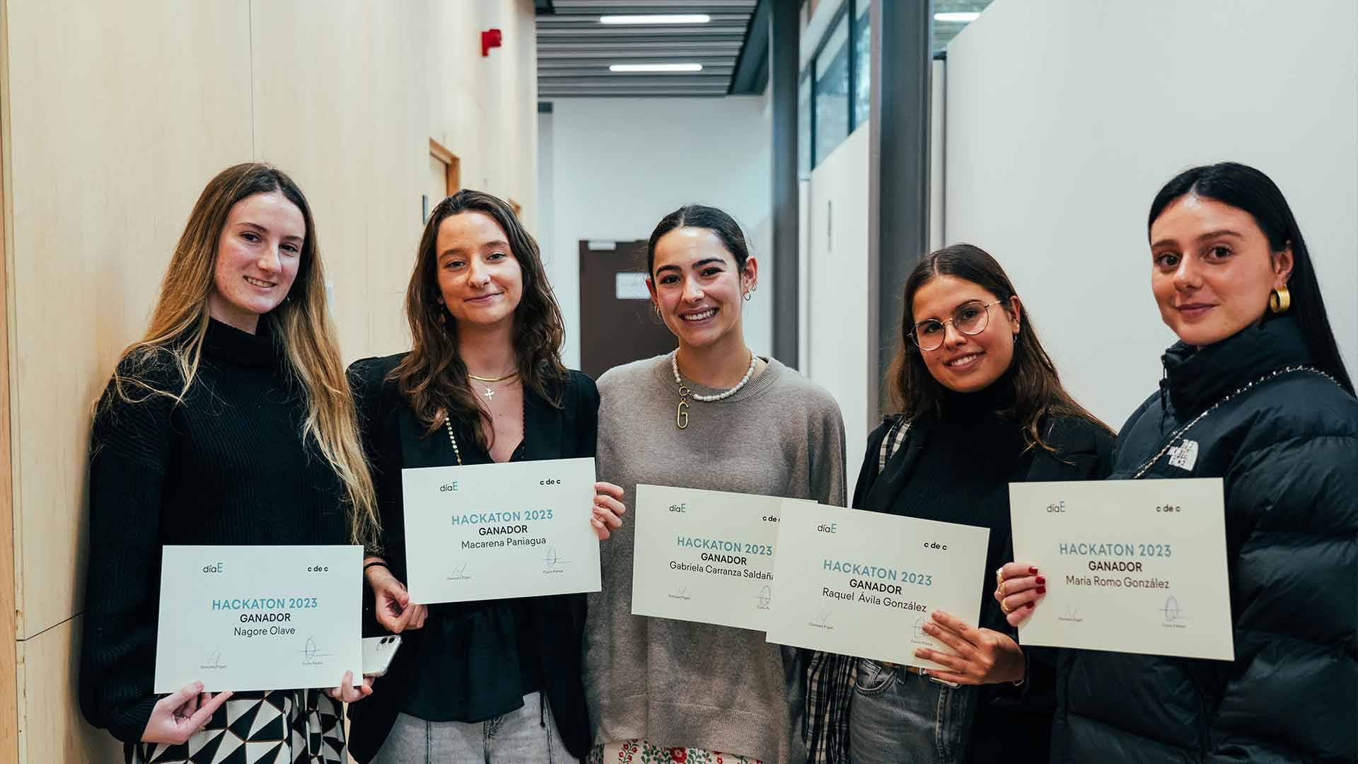 Un grupo de cinco mujeres posan con sus certificados de graduación en un ambiente académico.