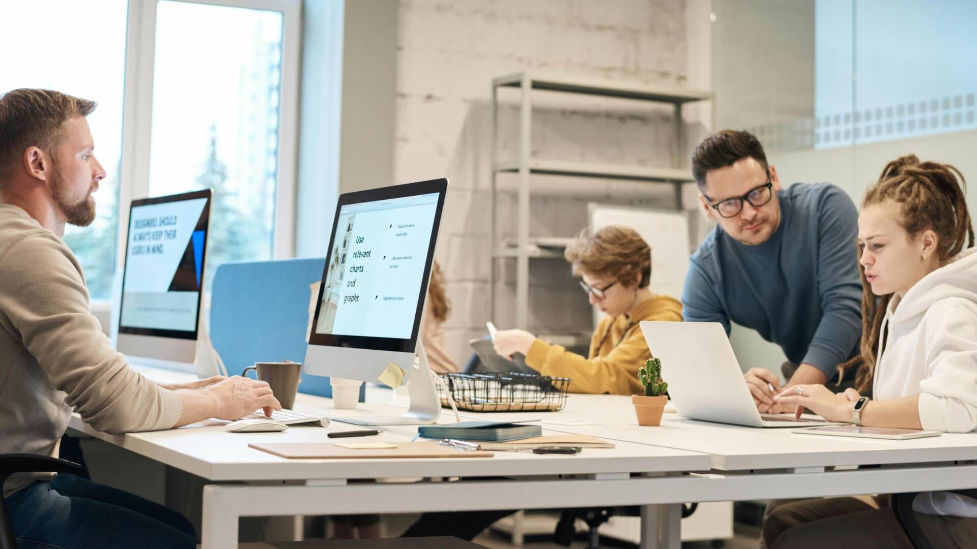Un grupo de personas trabaja en un espacio de oficina moderno con computadoras y dispositivos móviles.